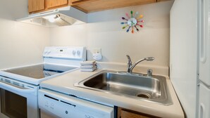 A kitchen with white appliances, a stainless steel sink, wooden cabinets, and a wall clock.