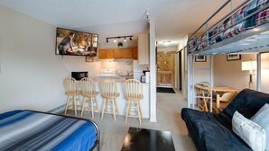 A compact studio apartment with a kitchenette, a dining area, and a living space with a sofa and a bed.