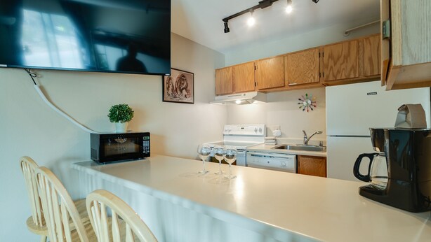 A modern kitchen with wooden cabinets, a white countertop, a microwave, a stove, and a coffee maker.