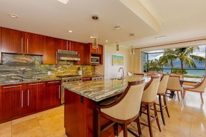 A modern kitchen with a large island, wooden cabinets, and a view of the ocean.