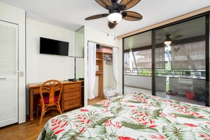 A bedroom with a bed, a desk, a chair, a wardrobe, a television, and a balcony with a view.