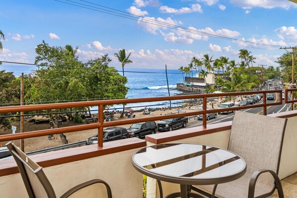 A balcony with a view of the beach, palm trees, and parked cars.