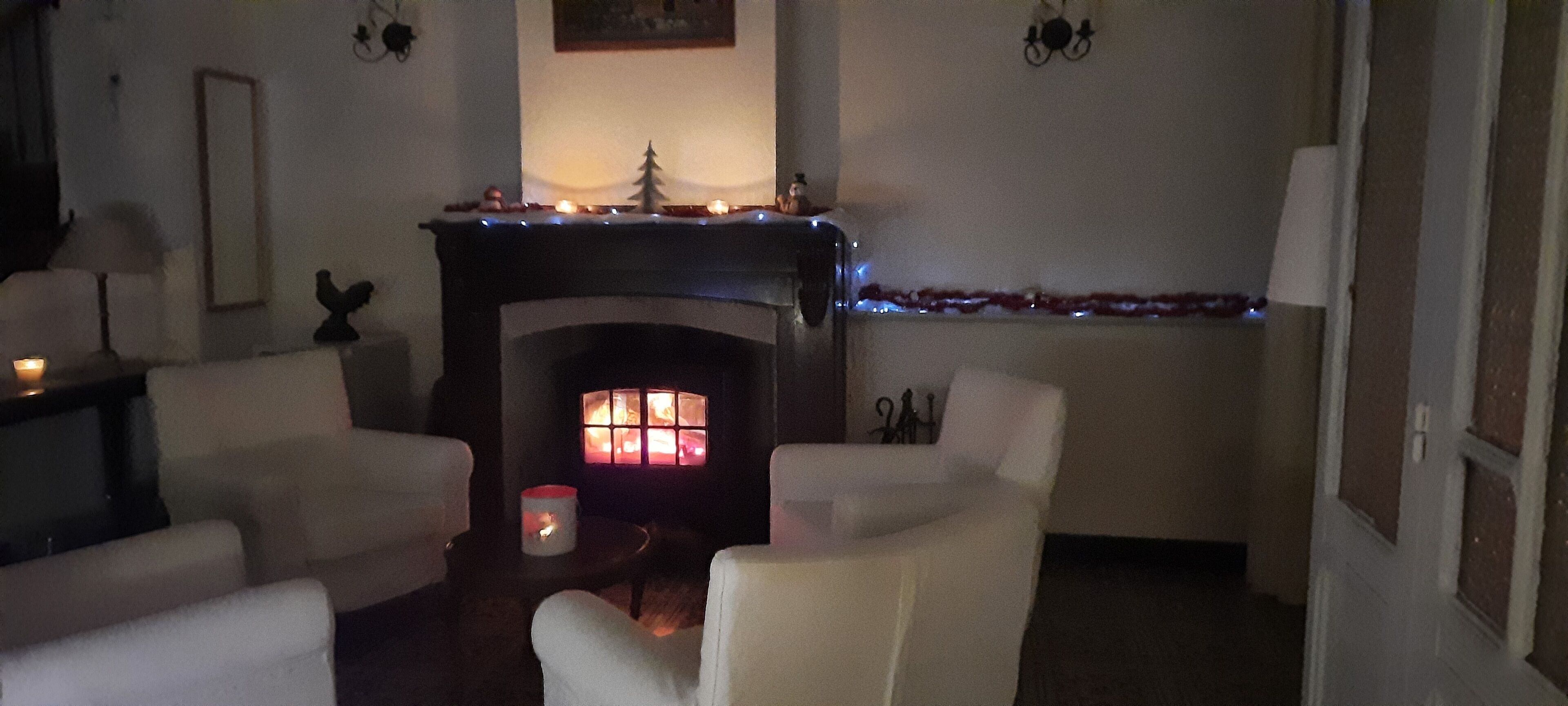 Un salon chaleureux avec une cheminée, des fauteuils blancs et une petite table sur laquelle est posée une bougie.