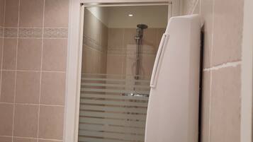 Un baño con baldosas color crema, ducha con puerta de vidrio y un toallero blanco.
