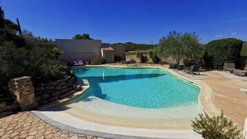 A swimming pool with a curved edge, surrounded by a paved deck and lounge chairs.