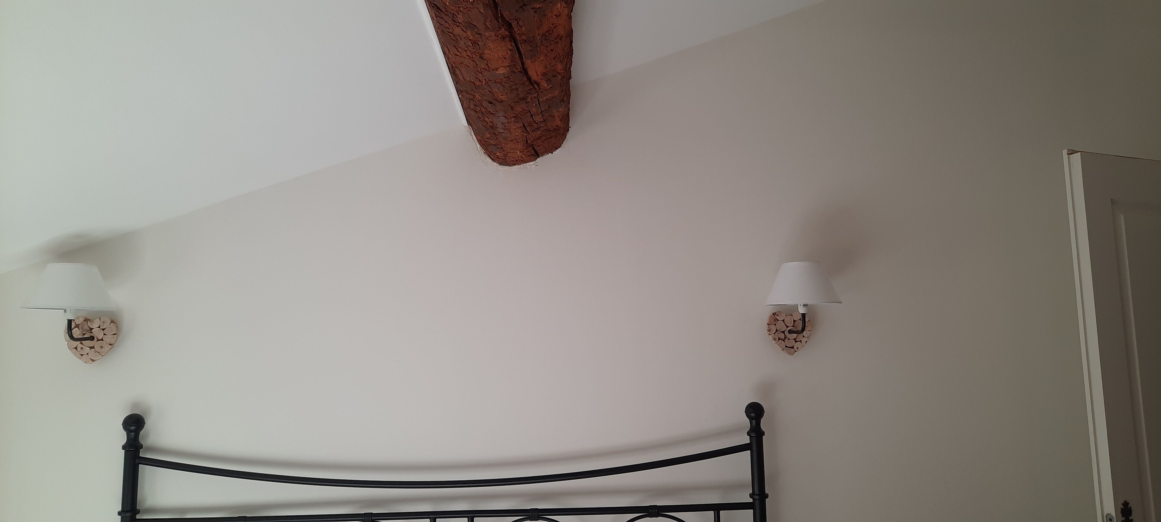 Una habitación con techo blanco, una viga de madera, dos lámparas fijadas a la pared y un cabecero de metal negro.