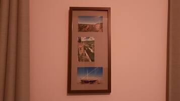 A framed photograph of a coastal landscape with cliffs and a boat on the shore, hung on a wall with brown curtains.