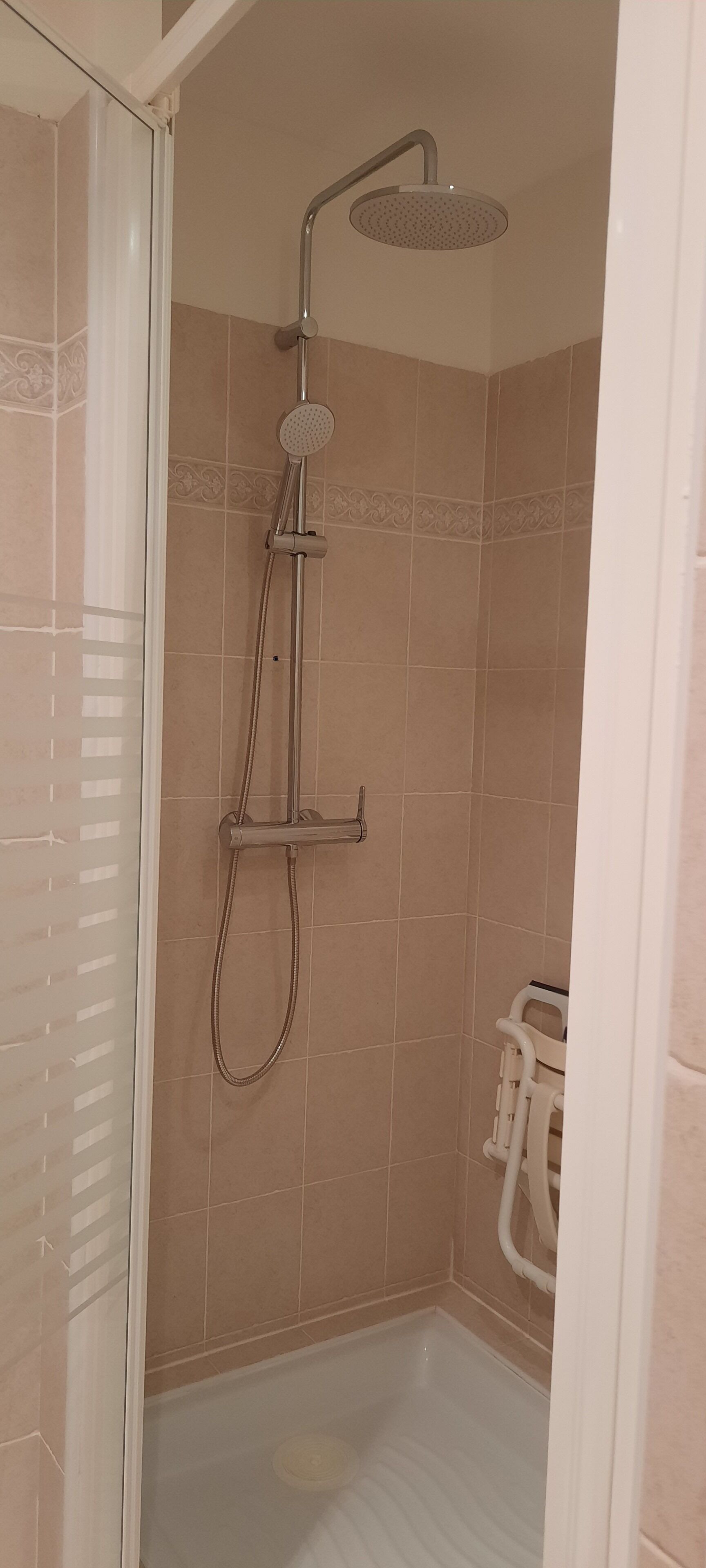 Zona de ducha con cabezal de ducha manual y grifo empotrado en la pared, paredes de azulejos y suelo blanco.
