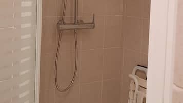 Zona de ducha con cabezal de ducha manual y grifo empotrado en la pared, paredes de azulejos y suelo blanco.