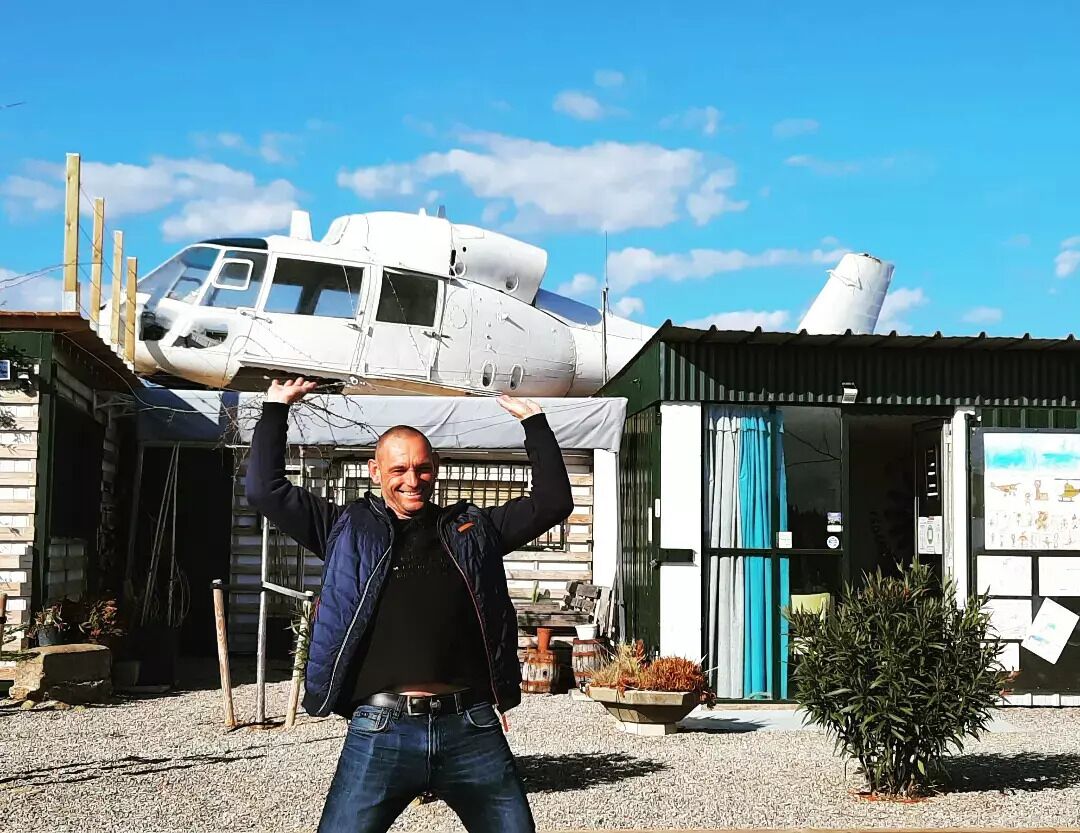 A man standing in front of a building with a helicopter parked outside.