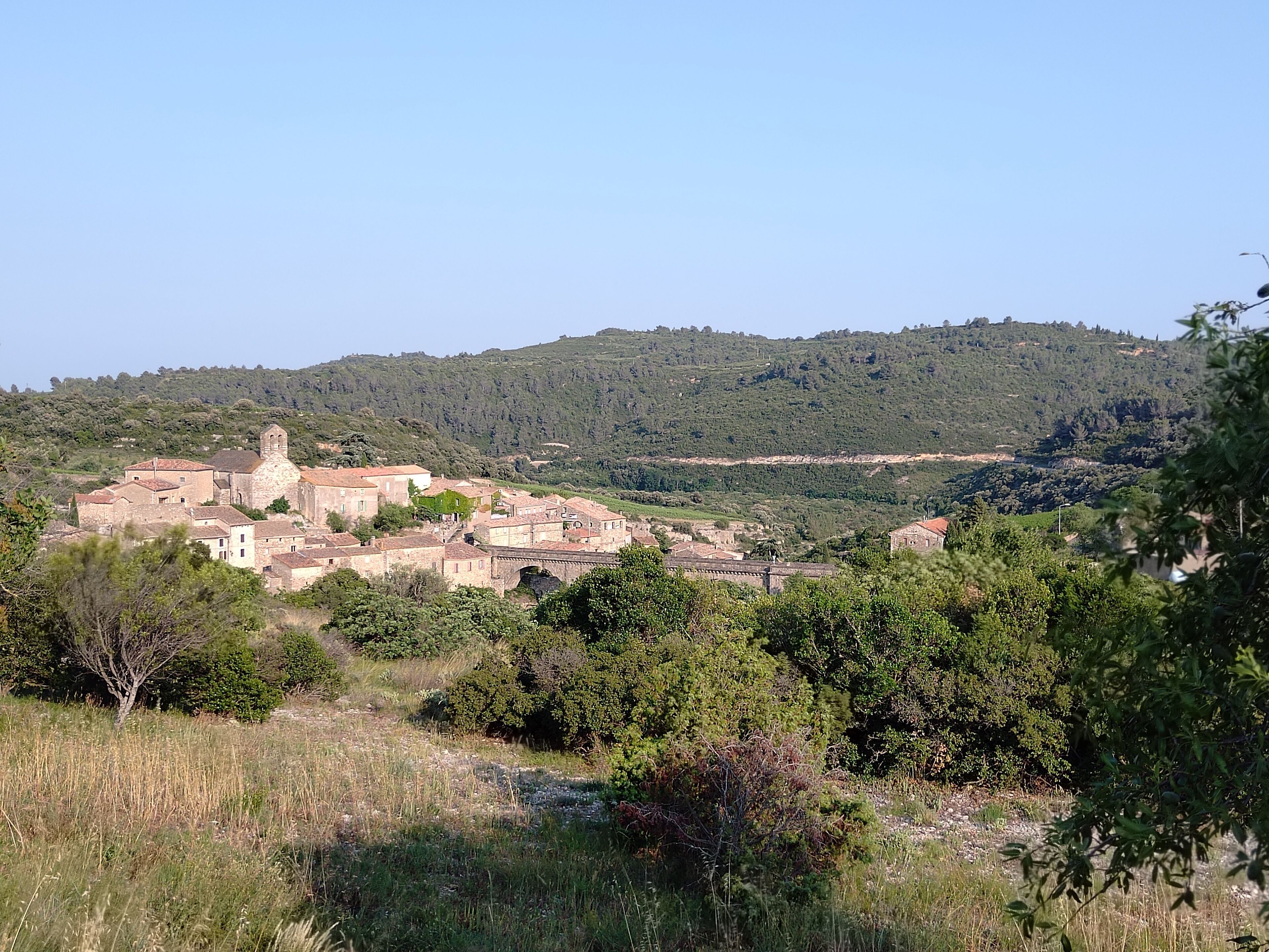 Un pueblo histórico con edificios de piedra y una iglesia, rodeado de vegetación y colinas.