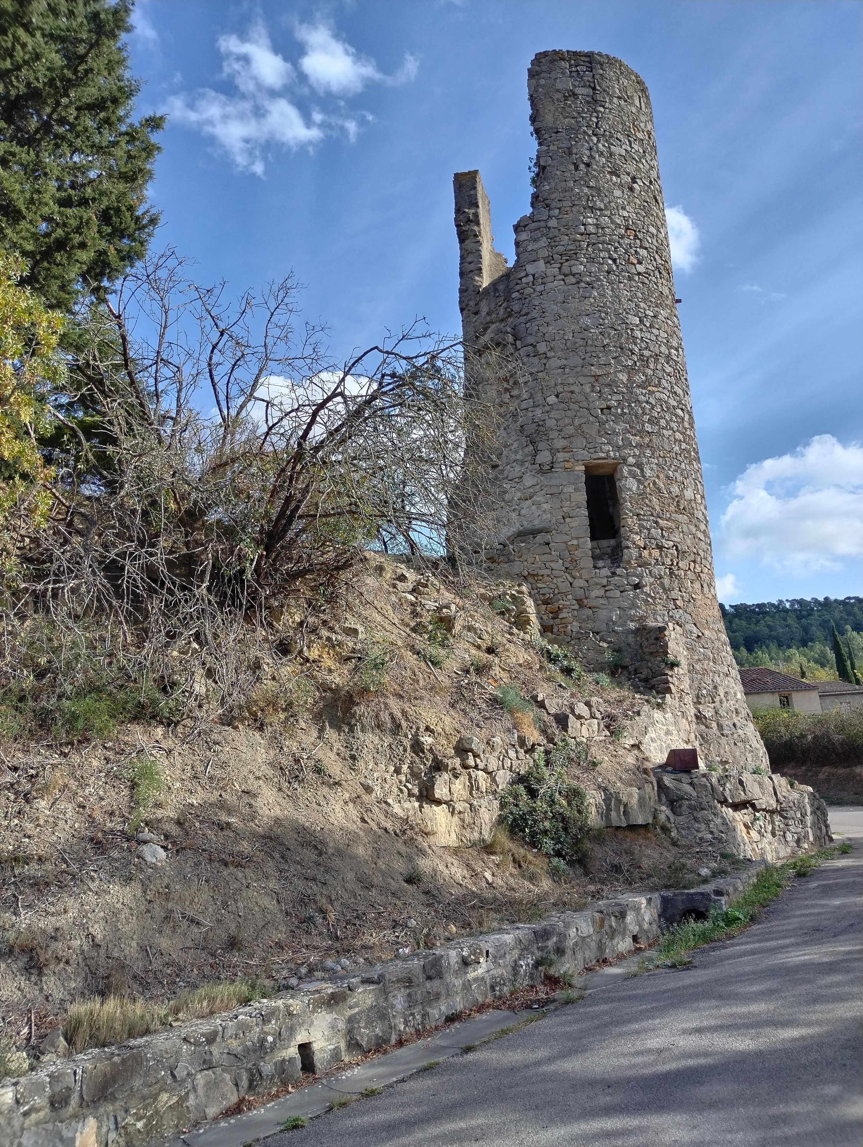 Les ruines d’une tour de pierre, avec une étroite ouverture, entourées d’une végétation desséchée et sous un ciel dégagé.