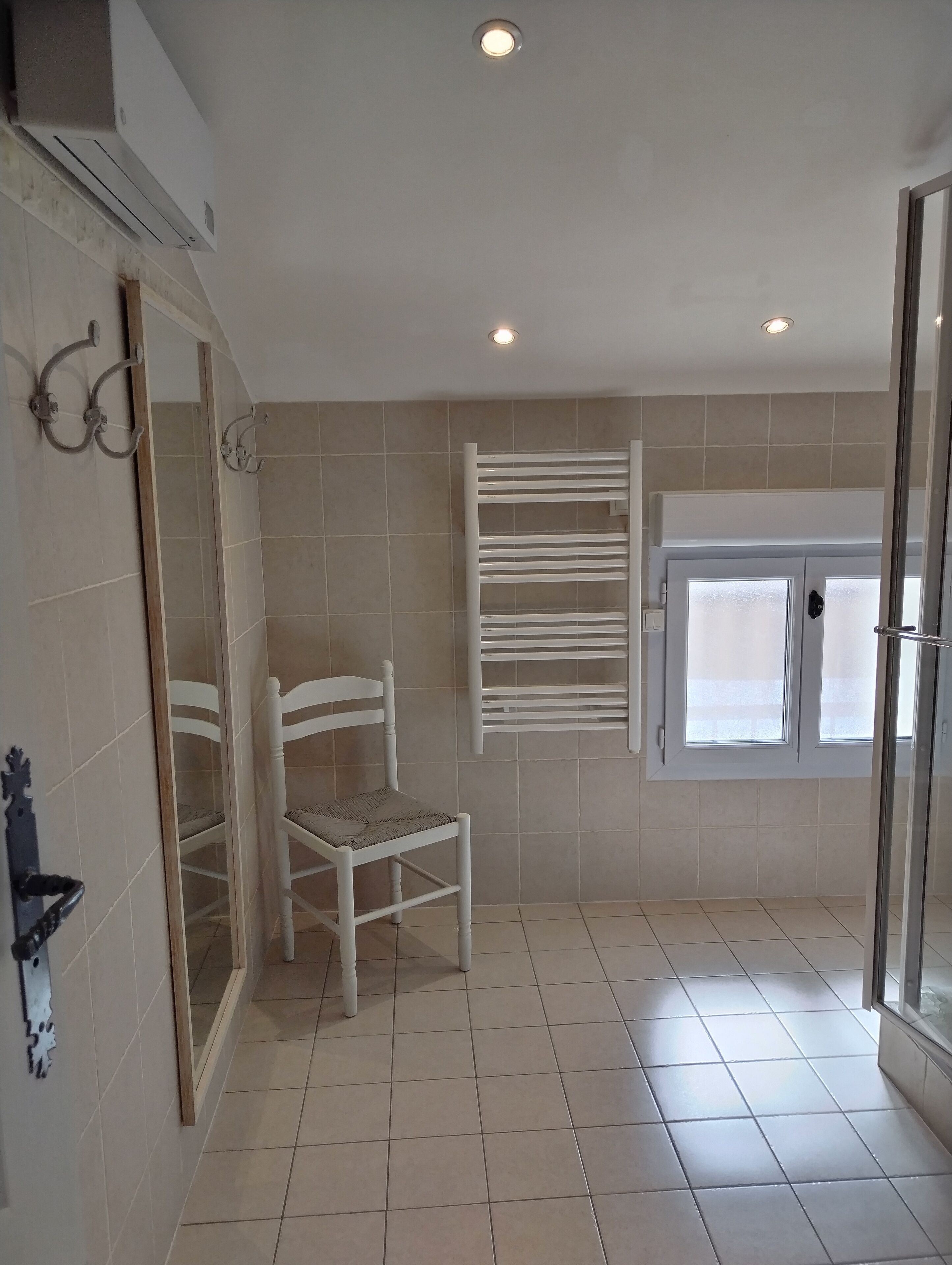 A bathroom with a white chair, a towel rack, and a glass shower door.