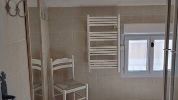 A bathroom with a white chair, a towel rack, and a glass shower door.