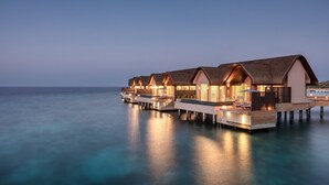 Watervilla's met open balkons, verbonden door looppaden, met uitzicht op een kalme zee.