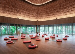 A spacious room with a high ceiling, large windows, and multiple red cushions on the floor.