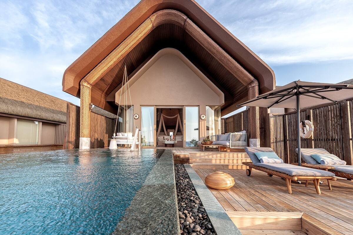 Un resort moderno con una amplia piscina infinita, terraza de madera y zona de estar exterior cubierta.