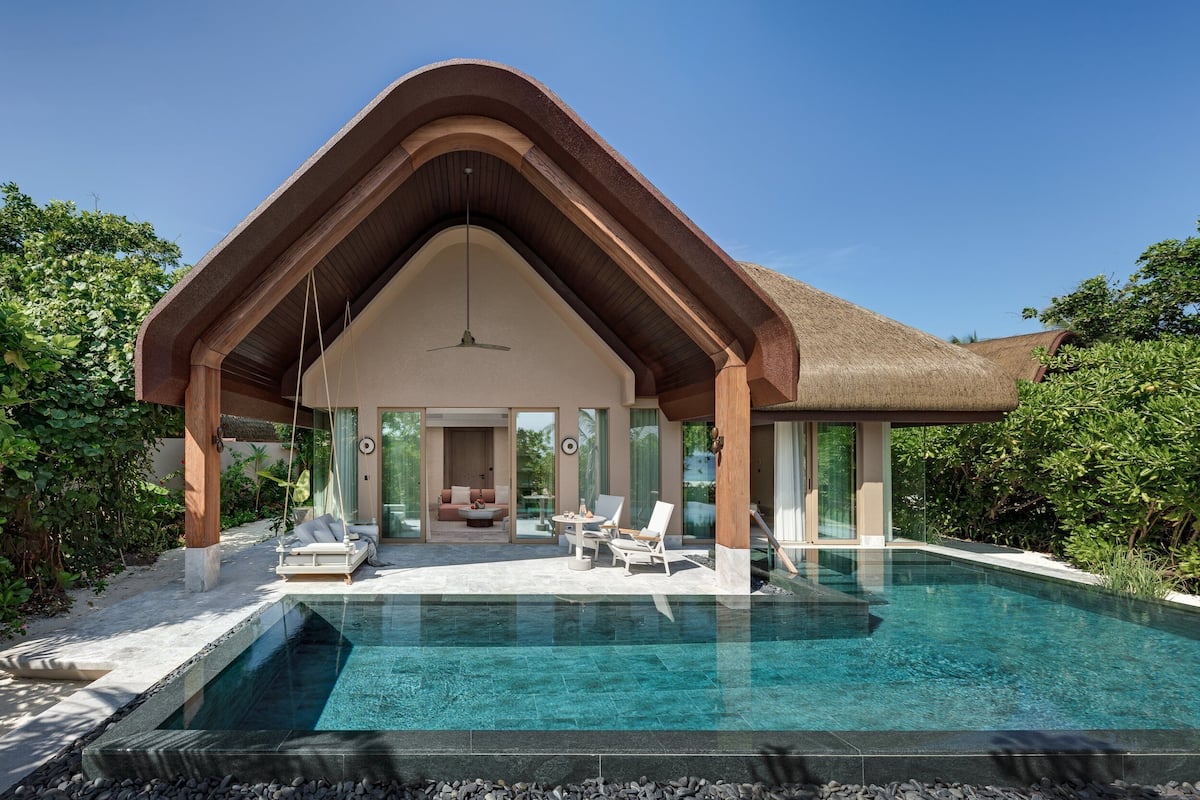 Una casa moderna con una amplia piscina, un área de estar techada y abundante vegetación.