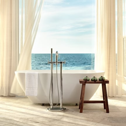 A bathroom with a bathtub, a shower, and a view of the sea through a large window.