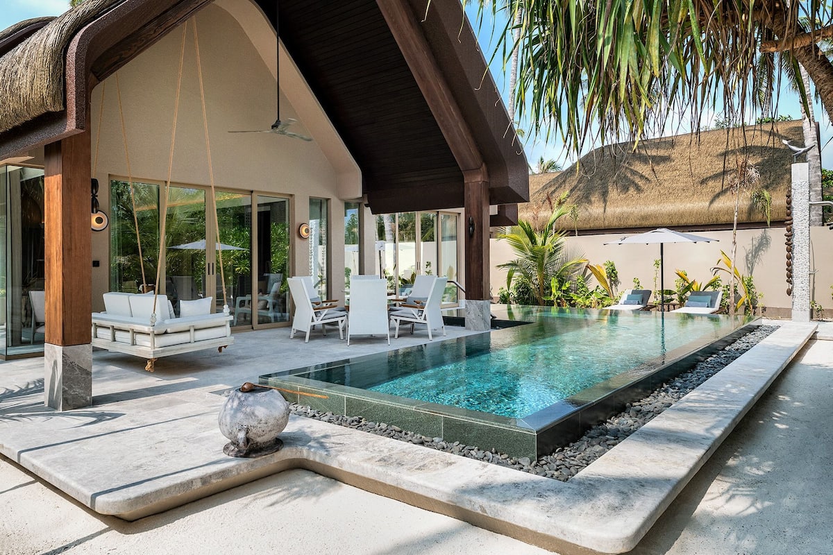 Un área de piscina moderna al aire libre con sillones de descanso y una zona de estar techada.