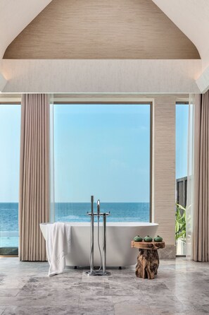 A modern bathroom with a freestanding bathtub, a towel rack, and a wooden table with teapots.