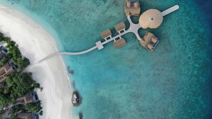 Luchtbeeld van een strandresort met een cirkelvormige indeling, inclusief een centraal gebouw met een koepeldak, verbonden door paden met verschillende rechthoekige gebouwen.