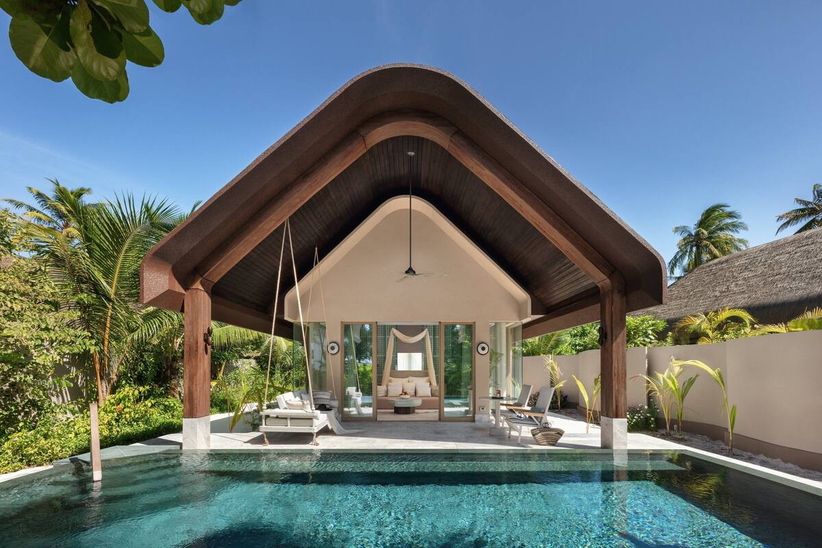 Una villa moderna con piscina, zona de estar cubierta y exuberante vegetación.