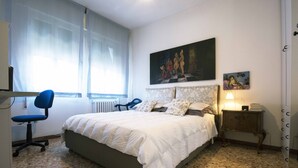 Una camera da letto con un letto, una scrivania, una sedia, un termosifone e una finestra con tende.