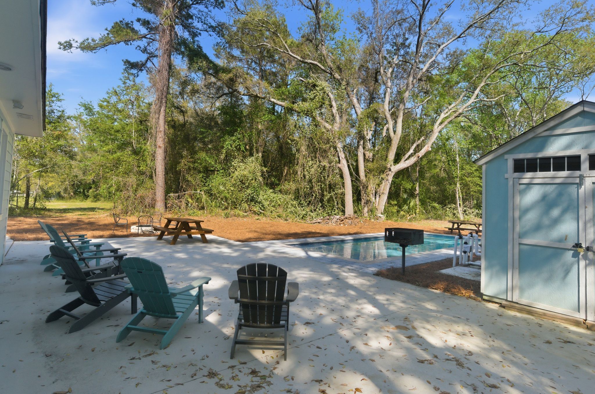 A backyard with a pool, Adirondack chairs, a picnic table, and a shed.
