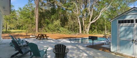 A backyard with a pool, Adirondack chairs, a picnic table, and a shed.
