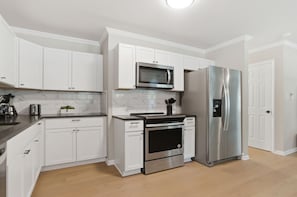 A modern kitchen with white cabinets, a stainless steel refrigerator, a microwave, and an oven.
