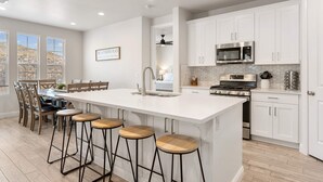 A modern kitchen with white cabinetry, a central island with stools, a built-in stove, and a microwave. - The Gather Place, LOADED WITH GAMES, DESERT VIEWS (Washington)