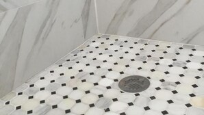 Ein Duschbereich mit einer weißen und grauen Marmorwand und einem gefliesten Boden mit geometrischem Muster.