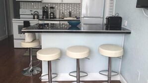 Eine Küche mit weißen Schränken, einer Mikrowelle, einem Herd, einem Kühlschrank und einer Bar mit Hockern.