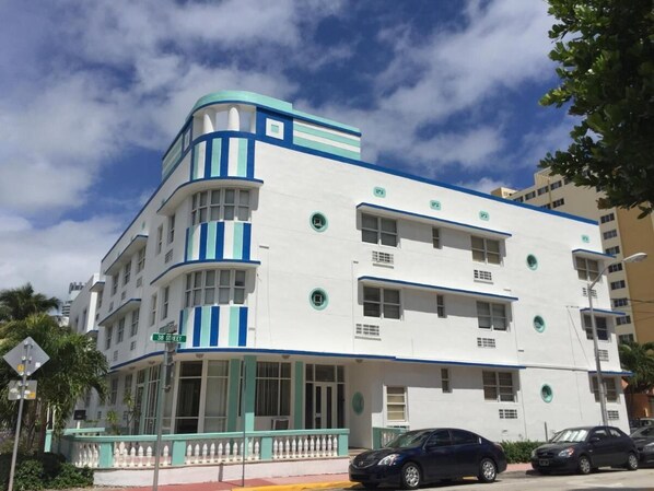 Un edificio de varios pisos con fachada blanca y detalles azules, que cuenta con ventanas amplias y una entrada en esquina.