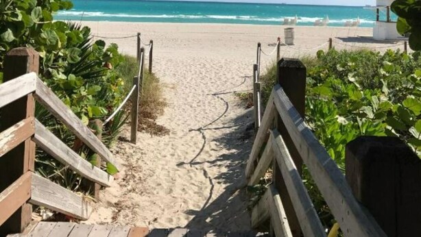 Ein Holzweg, der zu einem Strand führt, mit freiem Blick auf das Meer.
