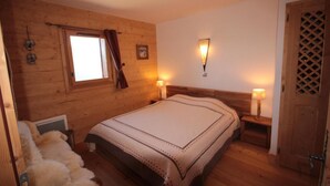 A cozy bedroom with a wooden headboard, a large bed, two bedside lamps, a window with curtains, and a wooden door with a lattice design. - 100m from ski slopes, 3rd floor, view panoramic, swimming pool, balcony, parking, tv, ski locker (Villard-sur-Doron)