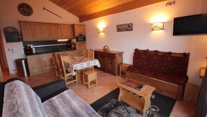 A cozy living room with a wooden sofa, a dining table with chairs, a kitchen area with wooden cabinets, and a flat-screen TV mounted on the wall. - 100m from ski slopes, 3rd floor, view panoramic, swimming pool, balcony, parking, tv, ski locker (Villard-sur-Doron)
