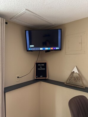 Ein Flachbildfernseher an der Wand, ein Willkommensschild und ein dekoratives Schild mit Bergmotiv.