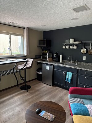 Eine kompakte Küche mit Mikrowelle, Toaster und Spüle. Ein Essbereich mit Tisch und Stühlen lädt zum Verweilen ein, daneben befindet sich eine kleine Sitzecke mit einer Couch.