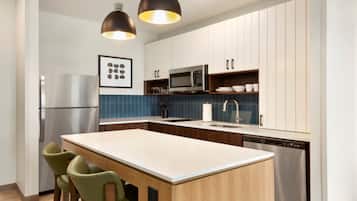 A modern kitchen with a central island, stainless steel appliances, and a blue tiled backsplash.