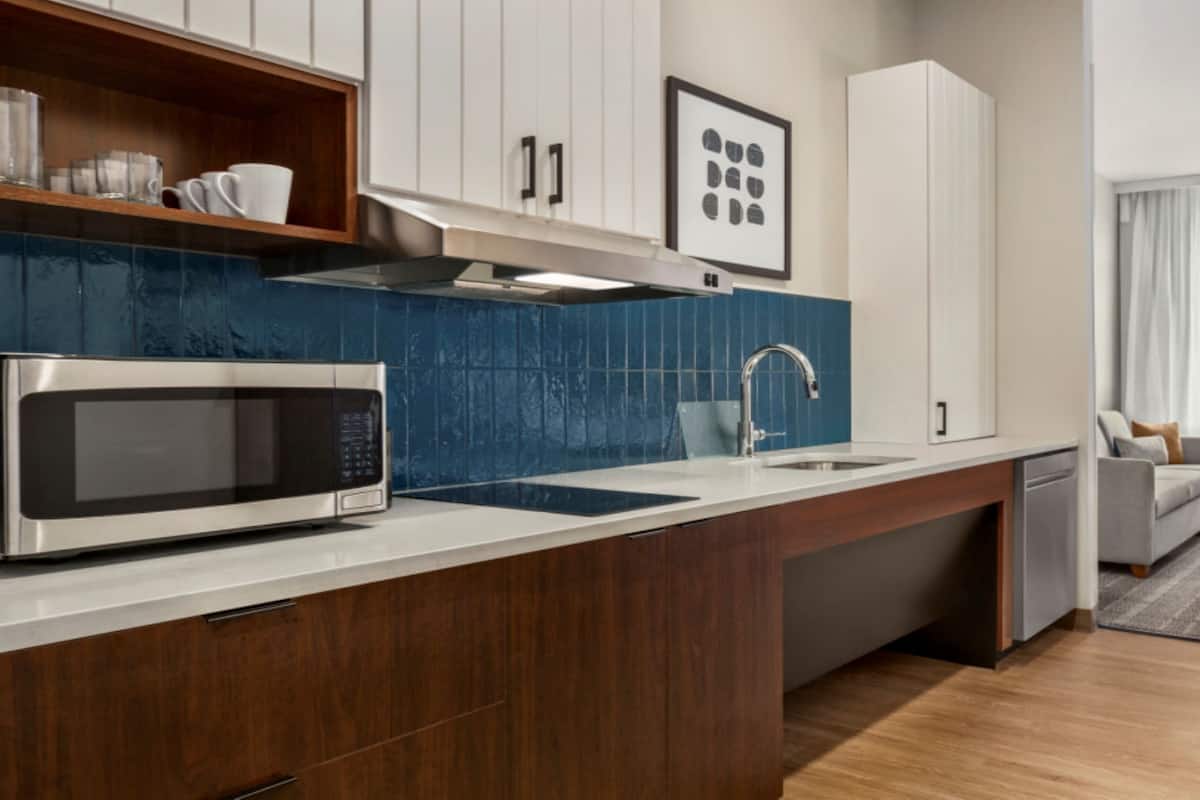 A modern kitchen with a built-in microwave, a sink, and a dishwasher. There is a wooden countertop and a blue backsplash.