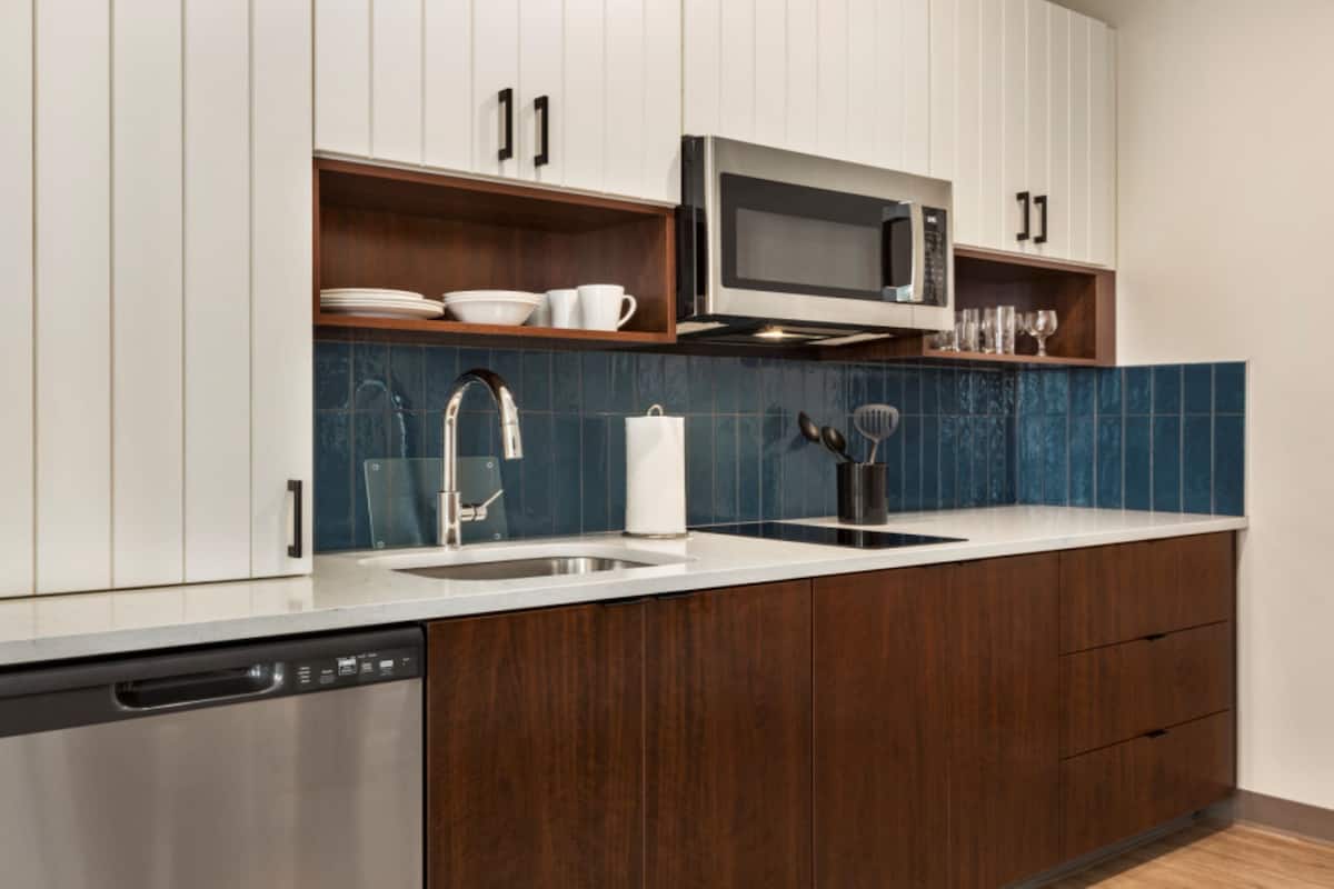 A modern kitchen with white cabinets, a stainless steel dishwasher, a microwave, and a blue tiled backsplash.