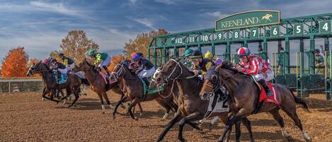 A horse race at Keeneland with jockeys on horses racing on a dirt track.