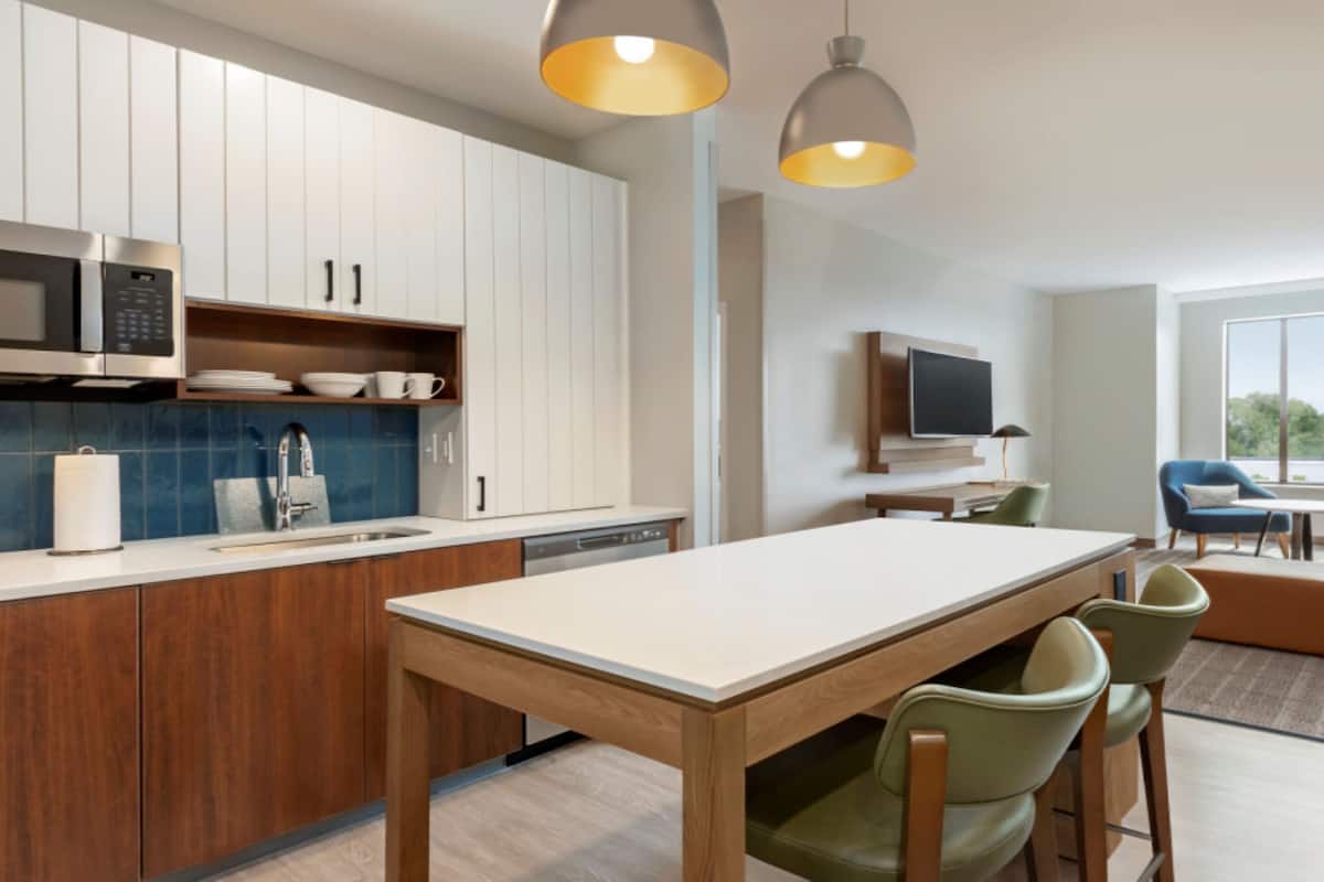 A modern kitchen with white cabinets, a built-in microwave, and a dining area with a wooden table and green chairs.