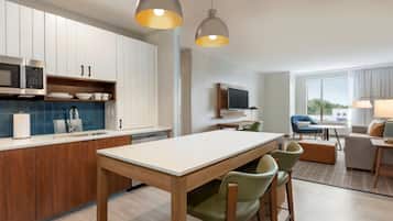 Una cocina moderna con armarios blancos, microondas integrado y un comedor con mesa de madera y sillas verdes.
