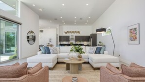 Una sala moderna con un sofá seccional, una mesa de centro y un comedor con armarios de madera oscura y una lámpara colgante.