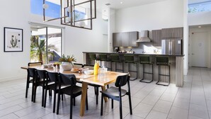 A modern kitchen with a central island, bar stools, and a dining area with a wooden table and chairs.