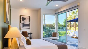 A modern hotel room with a large bed, a ceiling fan, a view of the outdoor pool area, and a framed artwork on the wall.