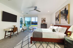 Ein modernes Schlafzimmer mit Bett, Schreibtisch und Stühlen, einem Deckenventilator sowie Bildern an den Wänden.